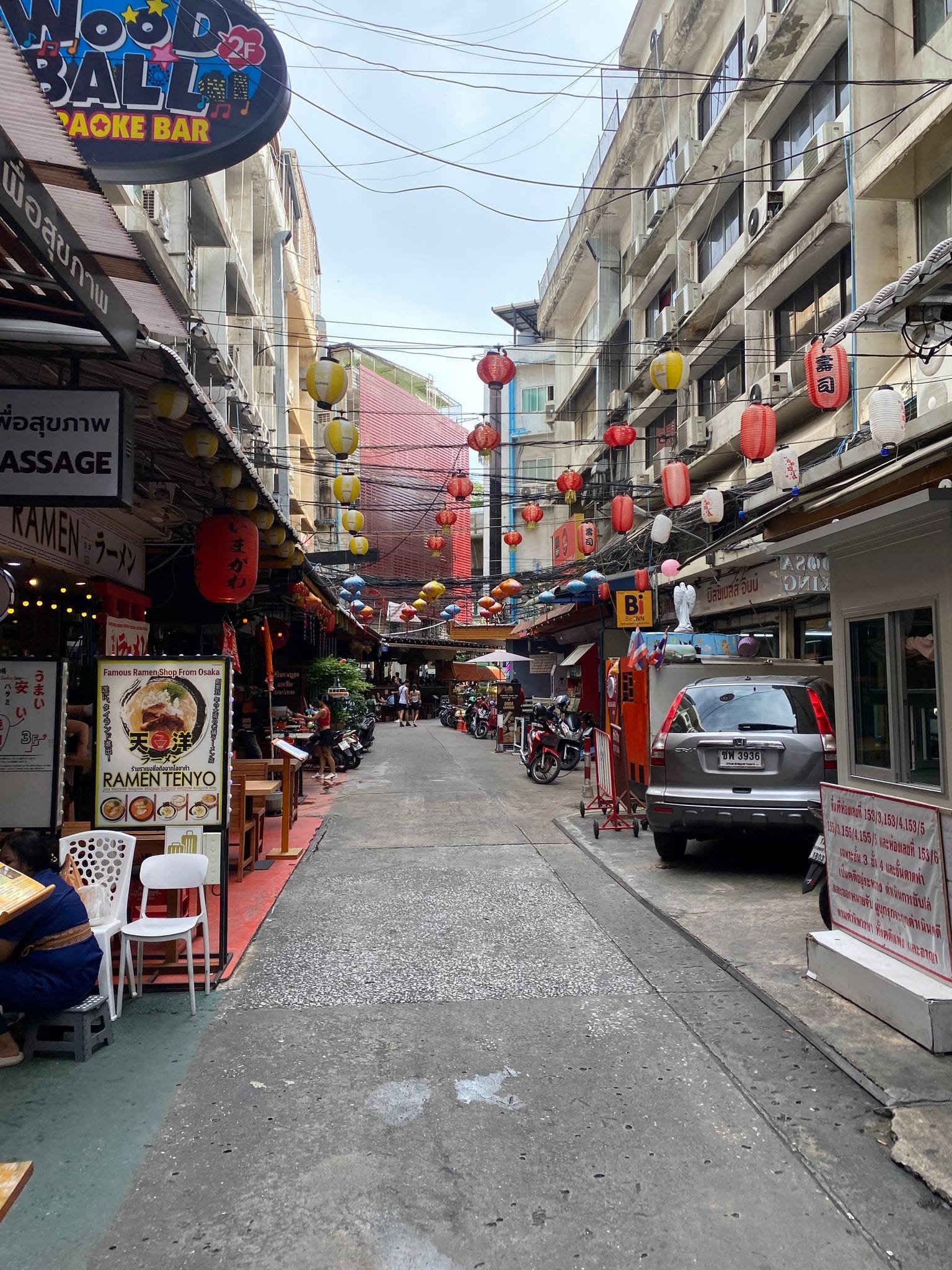 A Bangkok side street: tangled overhead cables, lanterns and parked scooters
