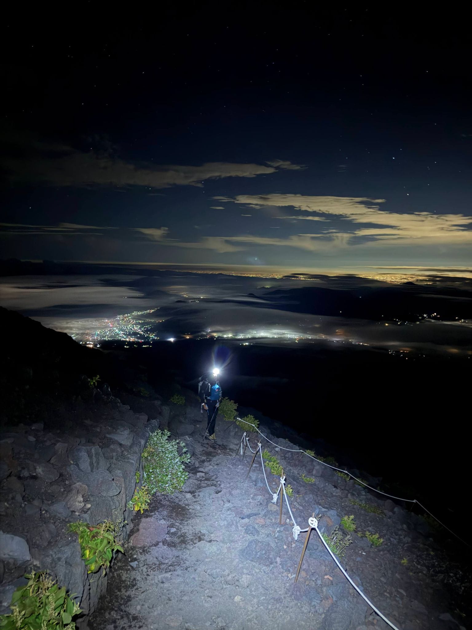 Headlamps on the trail before dawn, city lights below the clouds