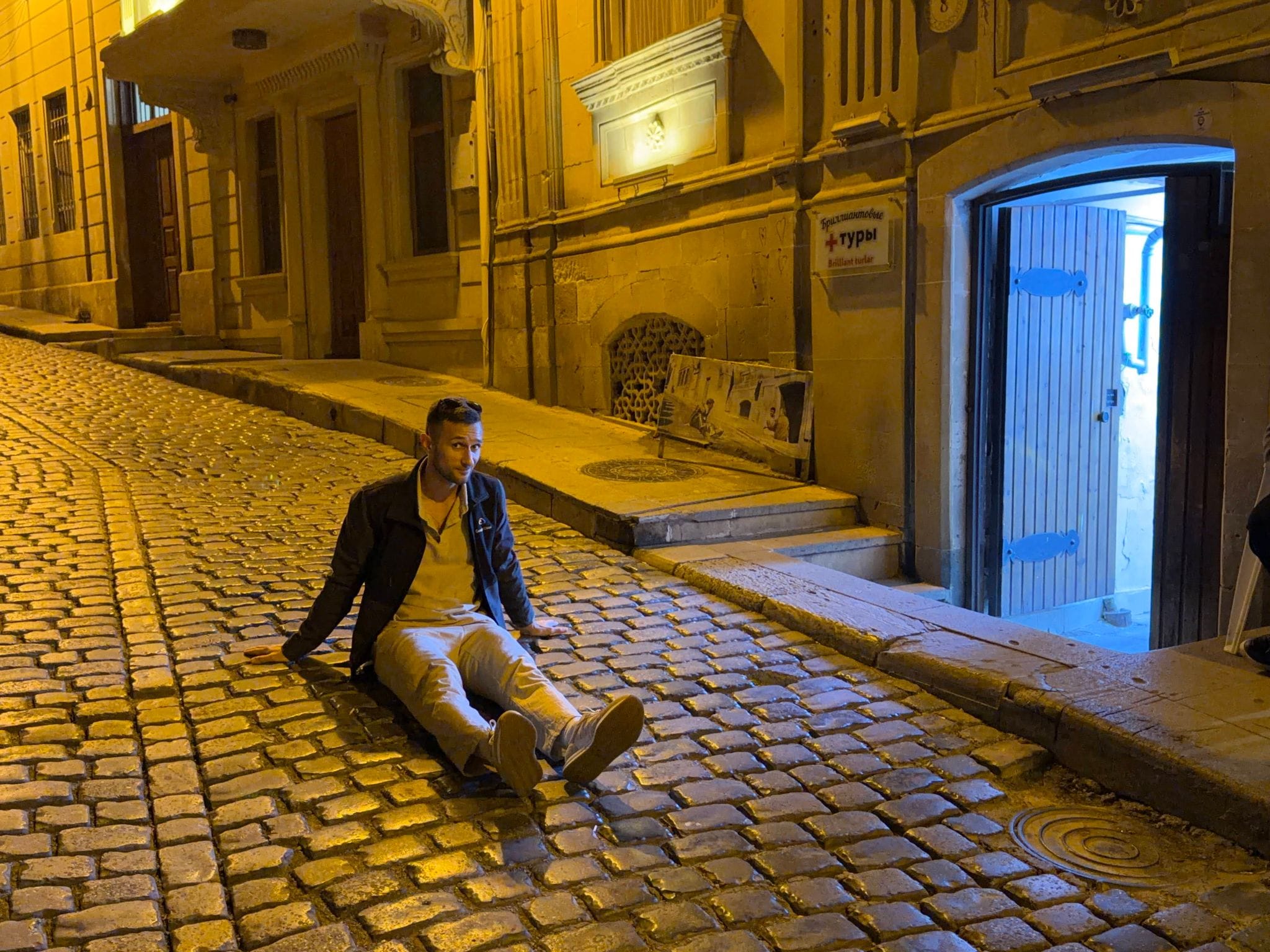 Nikita sitting on the cobblestones of Kichik Qala Street, recreating the fall scene from The Diamond Arm