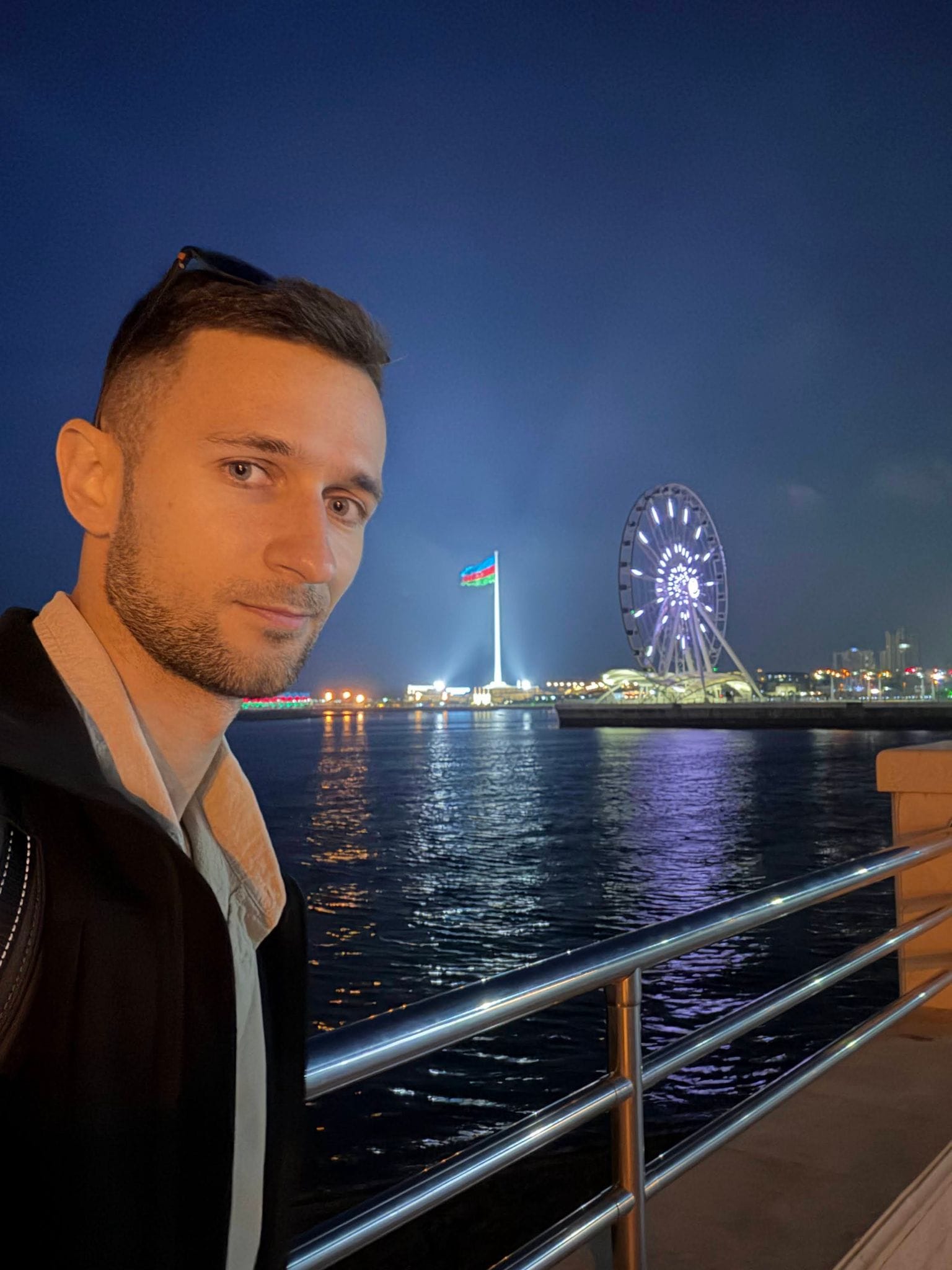 Night selfie on the boulevard with the Azerbaijani flag and the Baku Eye Ferris wheel across the water