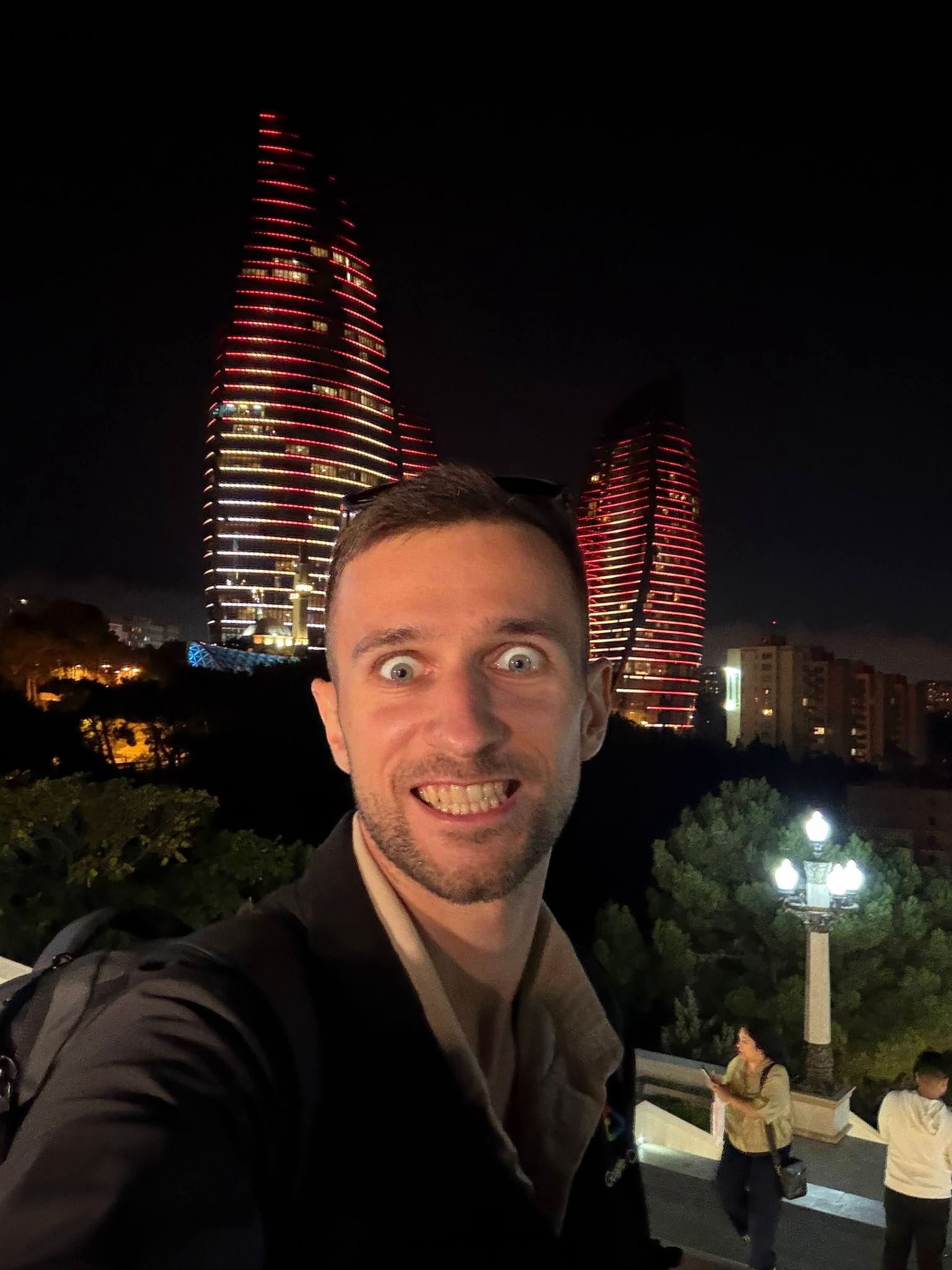 A grinning selfie with the red-lit Flame Towers behind, late in the evening