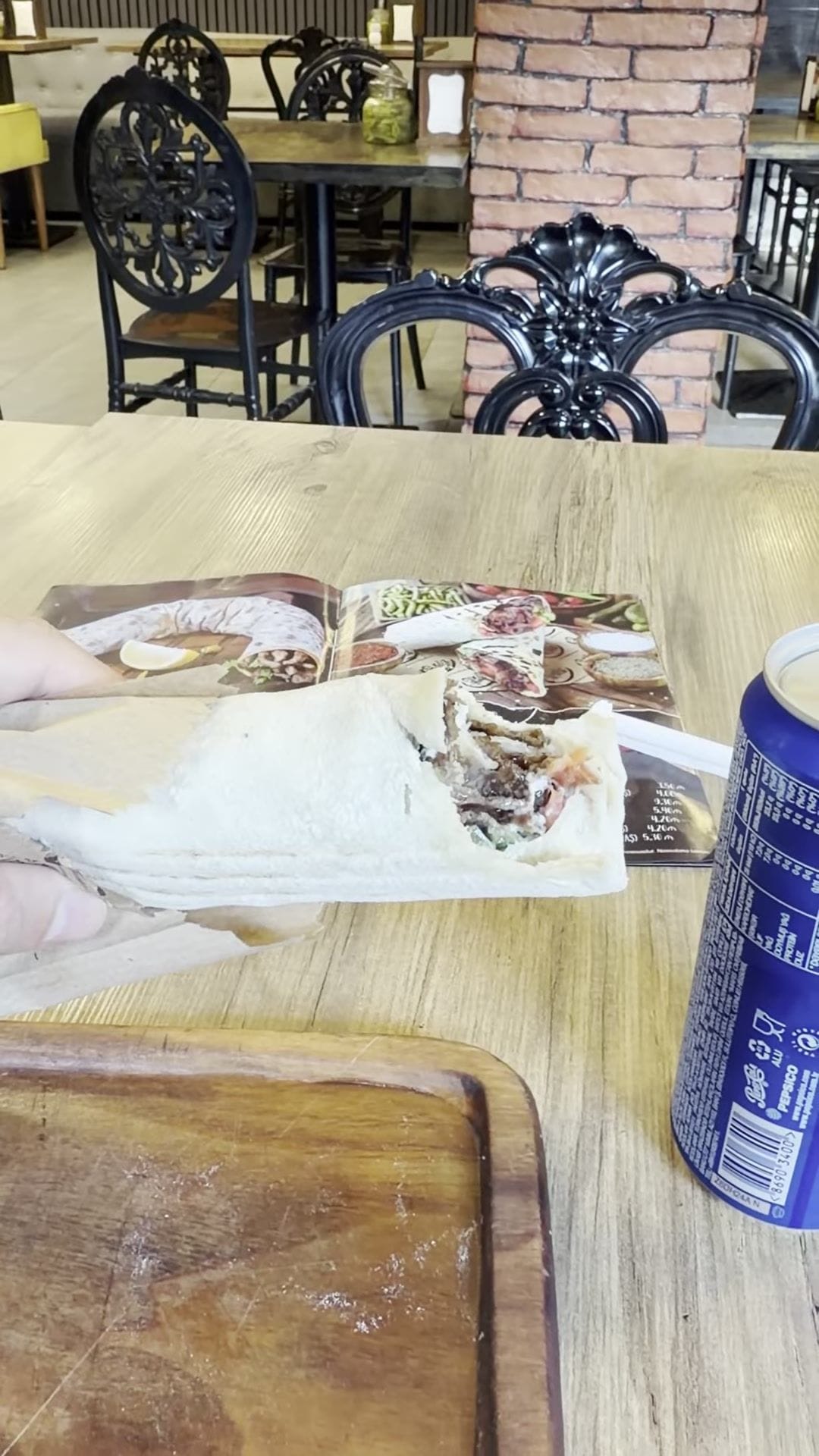 A shawarma wrap in thin lavash, cut open to show the layered meat, next to a can of soda in a Baku cafe